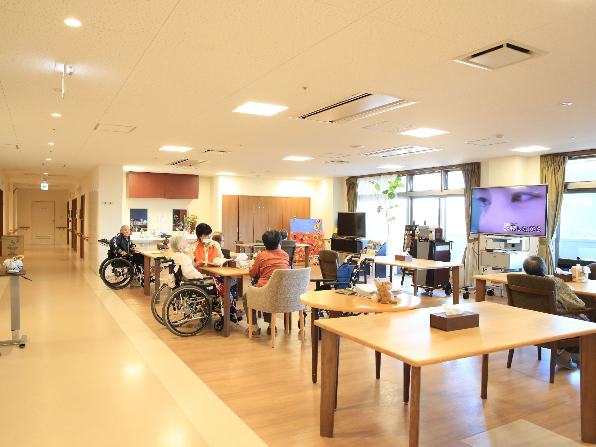 廊下の一角に広がる、開放的な間取りの食堂である。壁一面が窓になっていて明るい。大きなテレビが設置され、テーブルと椅子が並べられている。