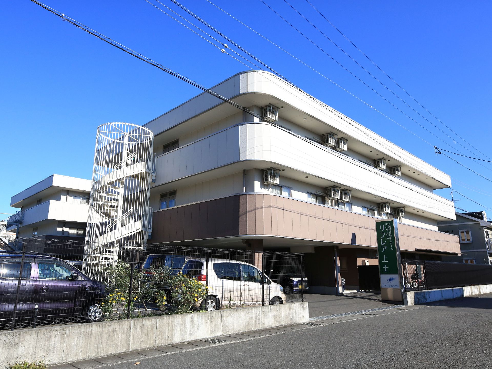 ３階建ての大きな建物で、すぐ横が駐車場になっている。建物の側面には、らせん状の非常階段が設置されている。