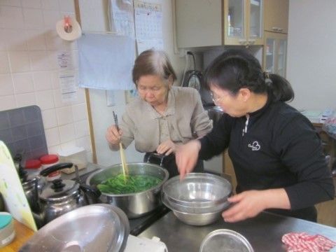 キッチンで野菜をゆでる高齢女性と女性スタッフ