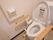 操作ボタンが取り付けられた洋式トイレである。便器の両サイドには、キャスターが付いたひじ掛けが置かれている。