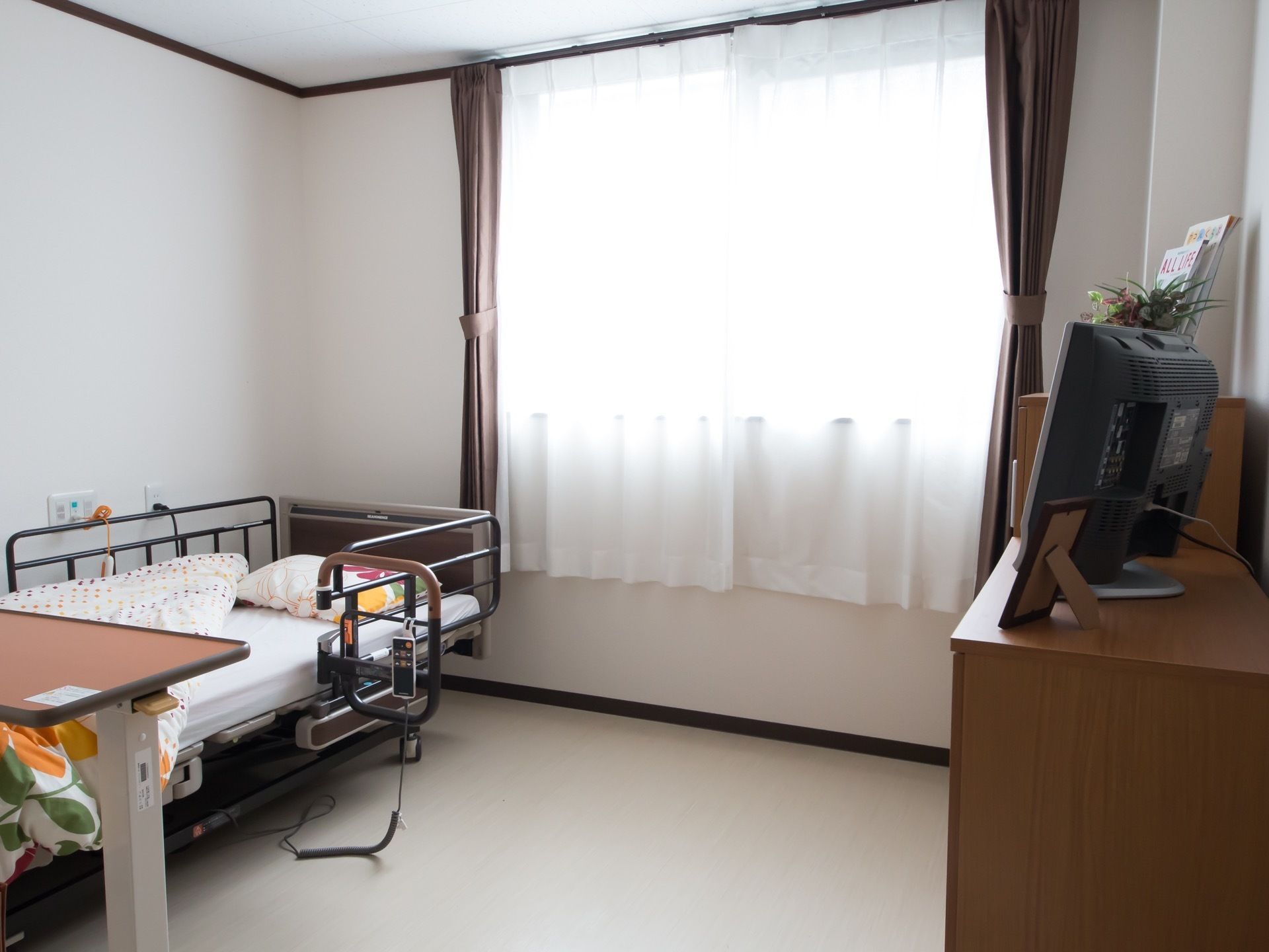 居室には窓が設置されている。介護用ベッドや可動式テーブル、チェストが配備され、暮らしやすくレイアウトされている。