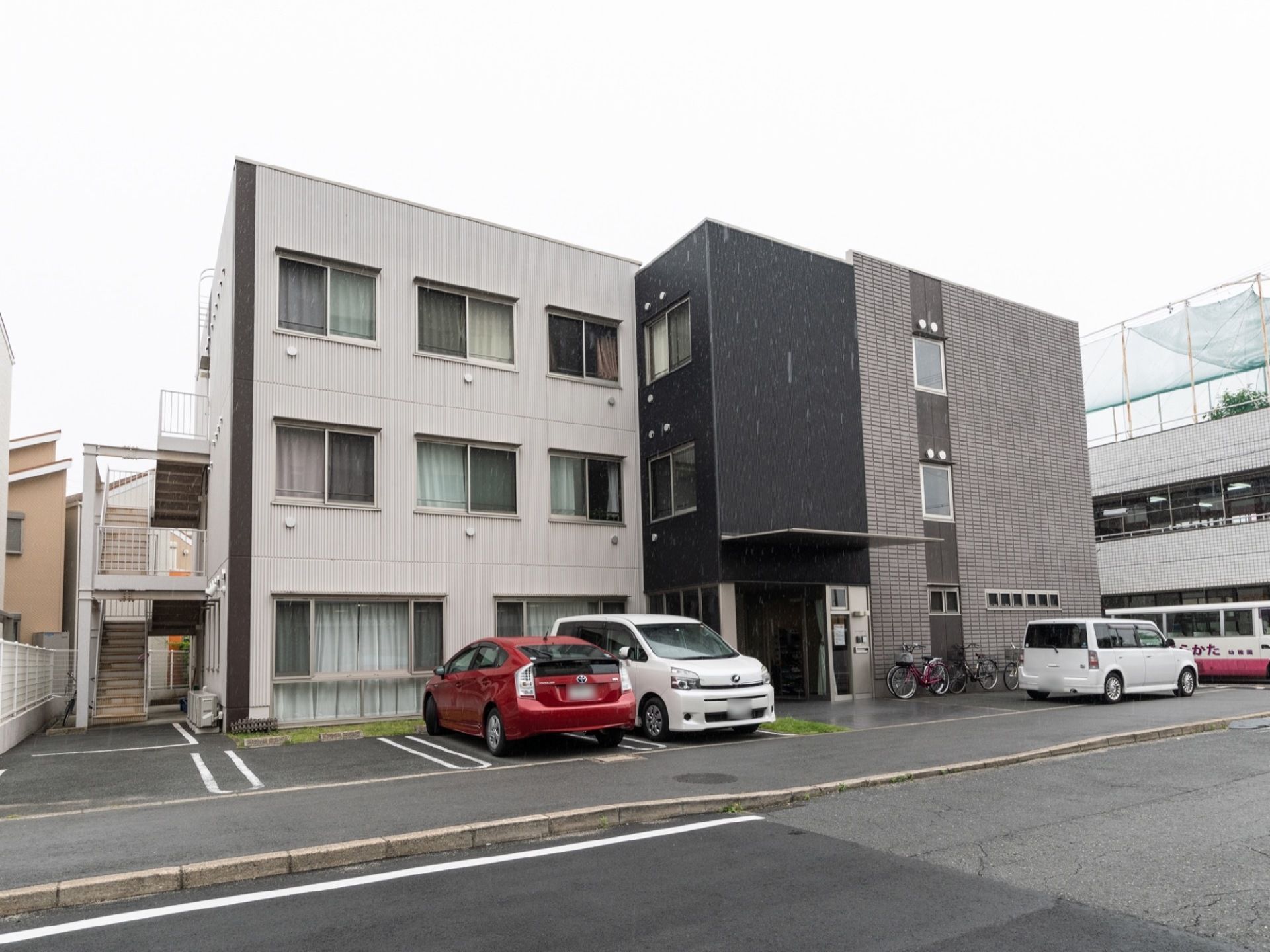 正面よりやや斜めから見上げた施設建物。玄関のある縦に黒い場所を境目に、左右で外壁のデザインが違っている。