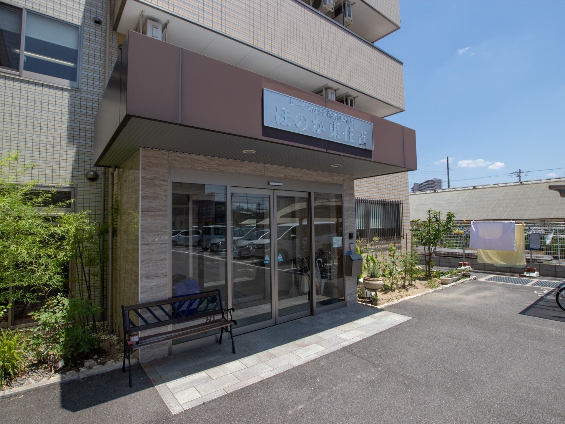 玄関は、ガラス張りの二重ドアを採用している。天井の側面に大きな看板を掲げている。傍にベンチを置き、横側に緑豊かな花壇を設けている。