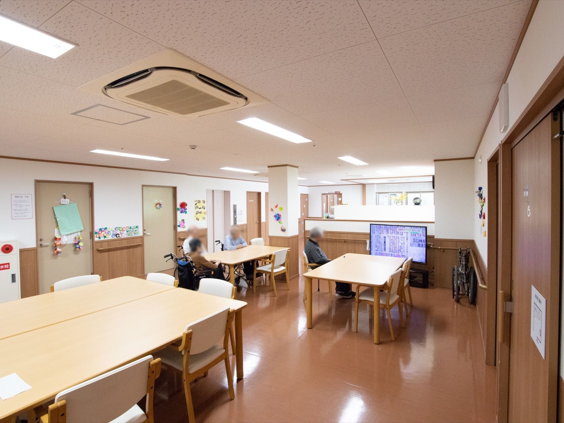 ダークブラウンの床に白木調のテーブルセットを並べている。壁に手作りのレイアウトを取り入れ、天井にエアコンを完備している。