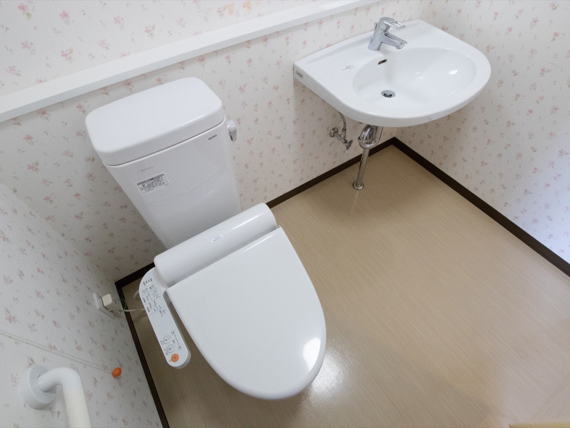 トイレ内は白を基調とした空間で、きれいで清潔感がある。洗面台が設置され、便座の横の壁には手すりと呼び出しボタンが設置されている。