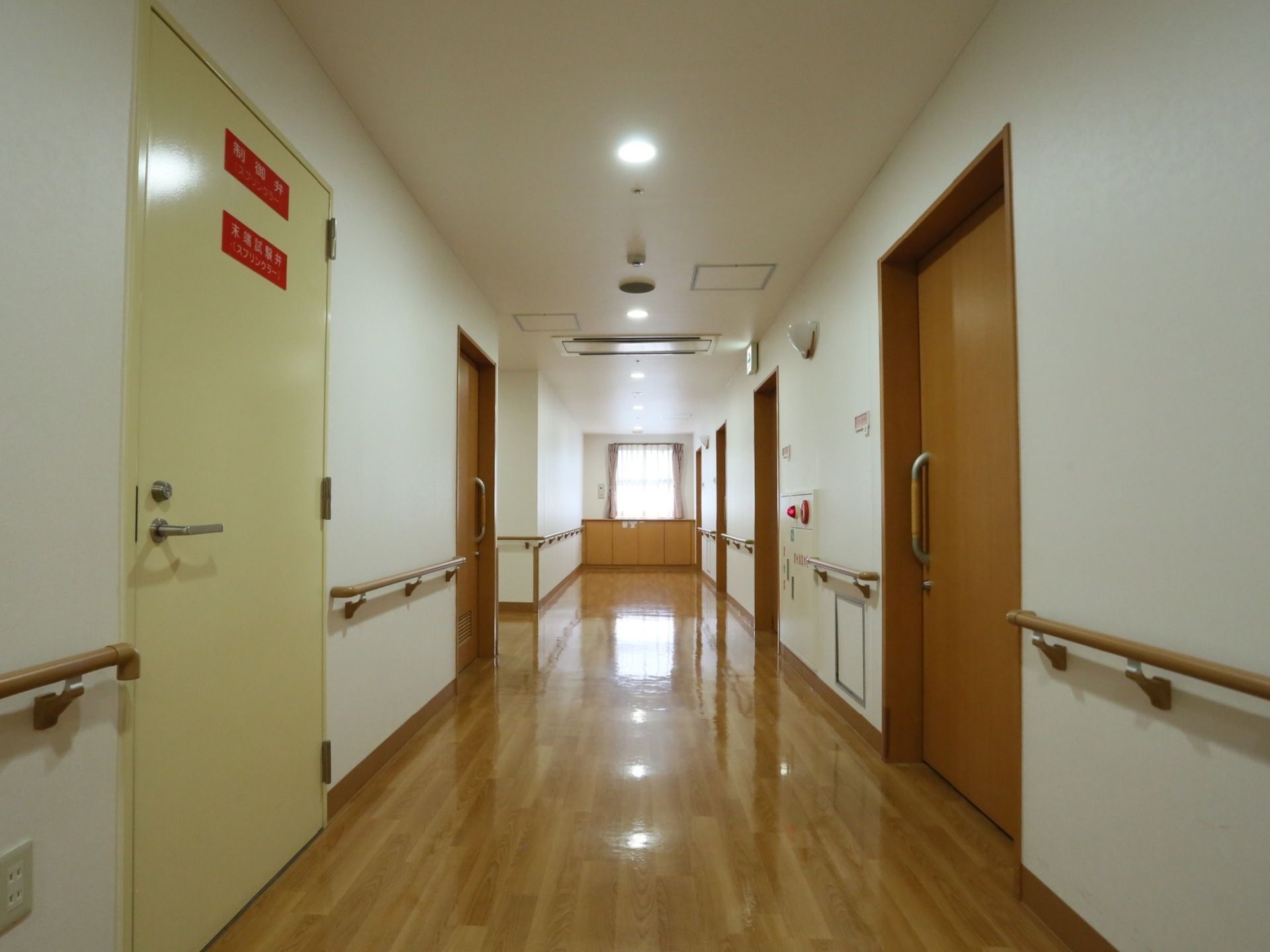 艶のあるフローリングの廊下が伸び、突き当たりは窓になっている。廊下の左右には居室の扉があり、合間は手すりが取りつけられている。
