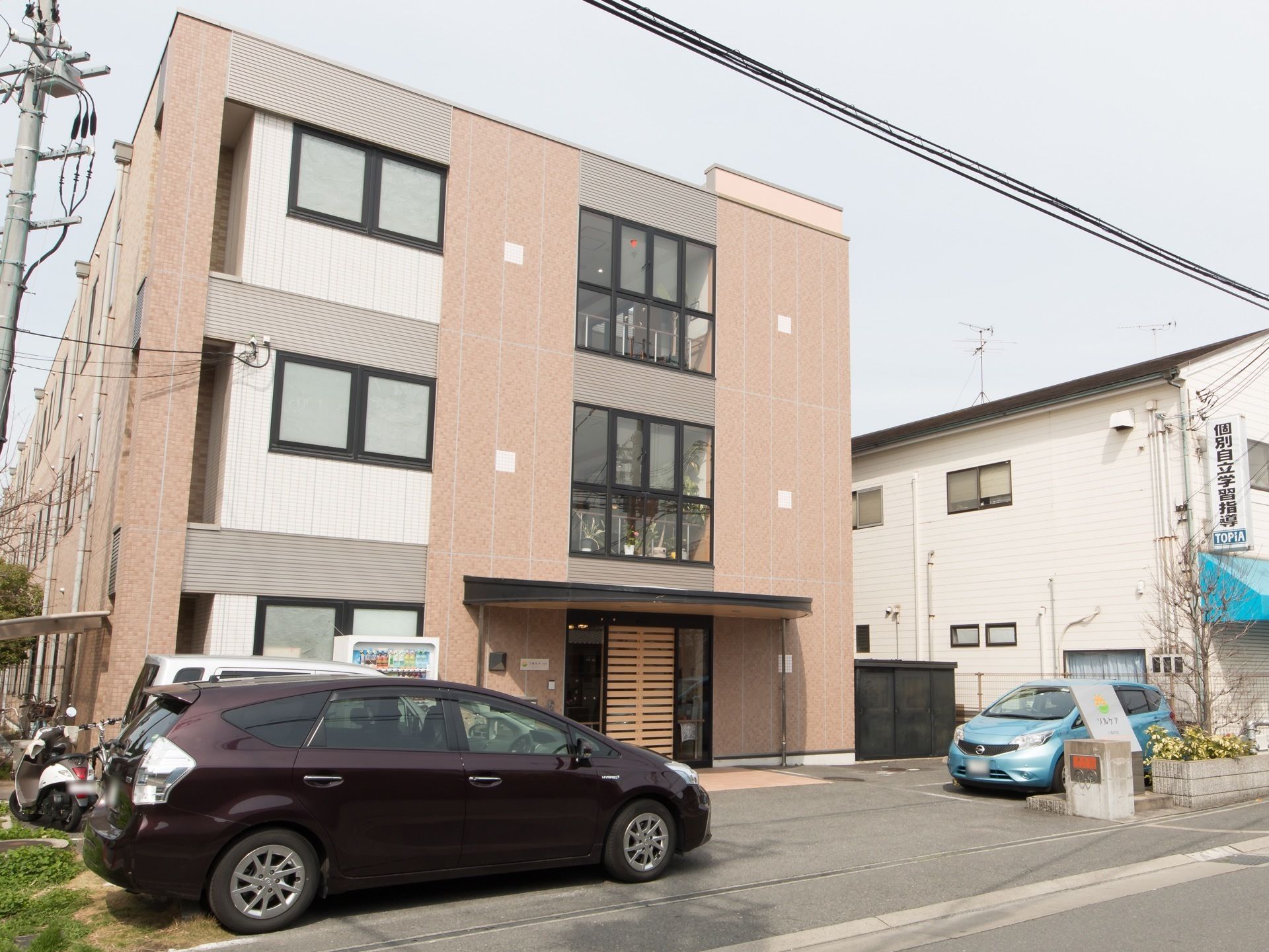 3階建ての建物で、玄関の上部には大きなひさしが設けられている。ドアの左側には自動販売機が1台設置されている。