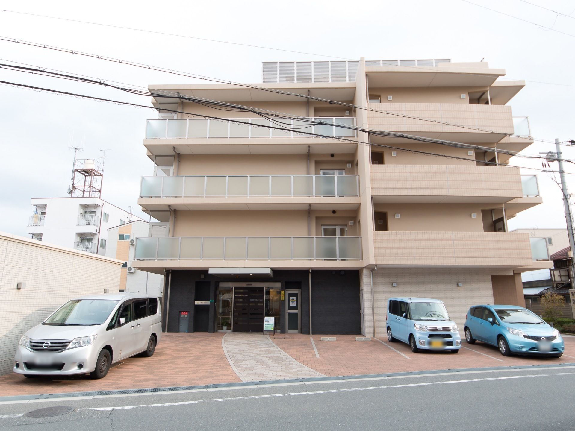 ベージュ色の外壁の４階建ての建物で、各階にベランダが設けられている。ベランダには安全のため柵が設置されている。
