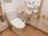 左側の壁に備えつけの手すりが、右側に可動式の手すりが取りつけられた個室トイレで、床はフローリングになっている。