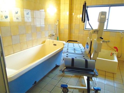 仰臥位入浴用のストレッチャーがある。壁面は黄色いタイルが張られており浴槽の青と合わせて元気の出る色合いである。