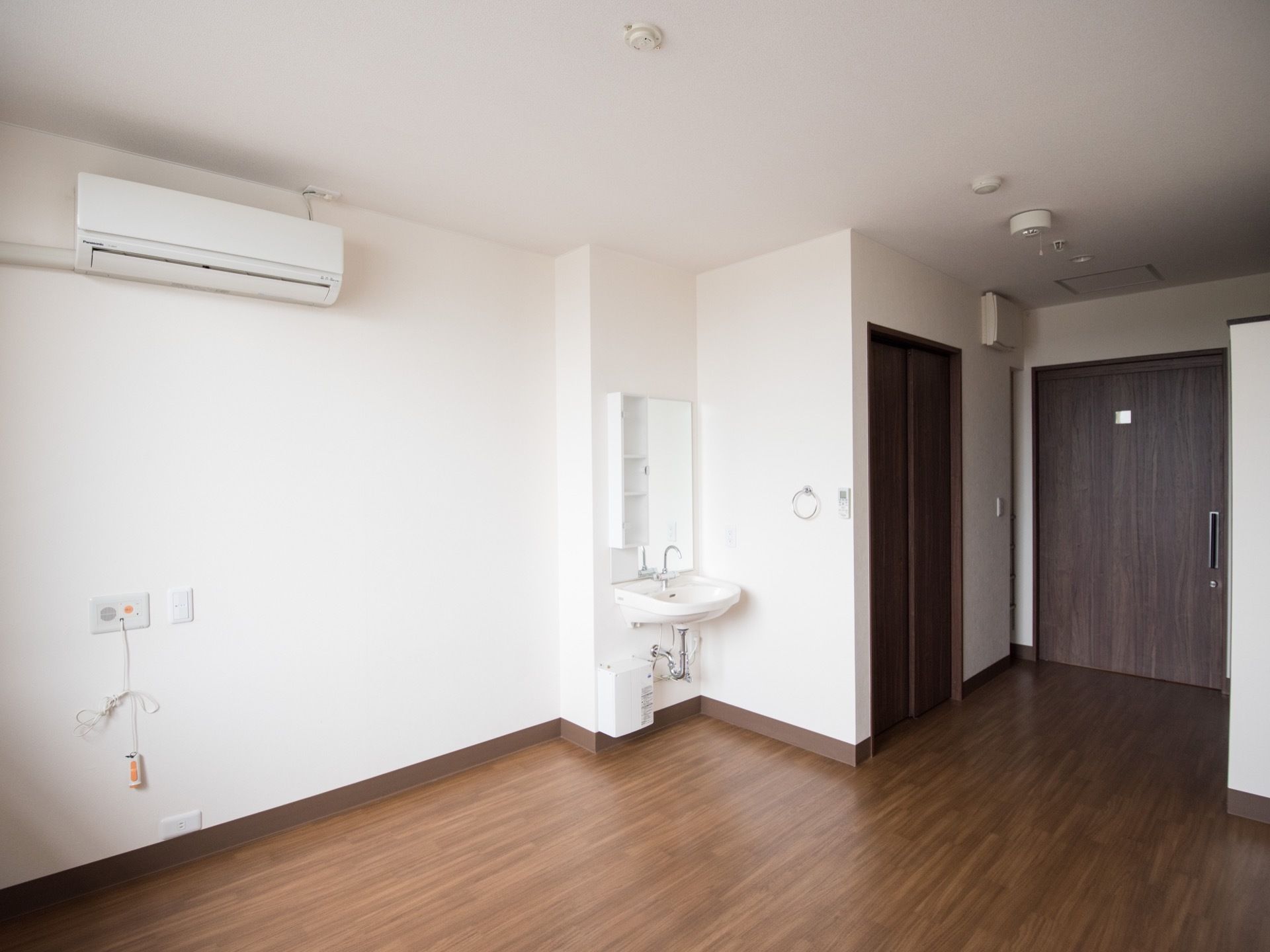 居室内は、真っ白な壁とダークブラウンの床とのコントラストが美しい。トイレや洗面設備、エアコン、ナースコールが完備されている。