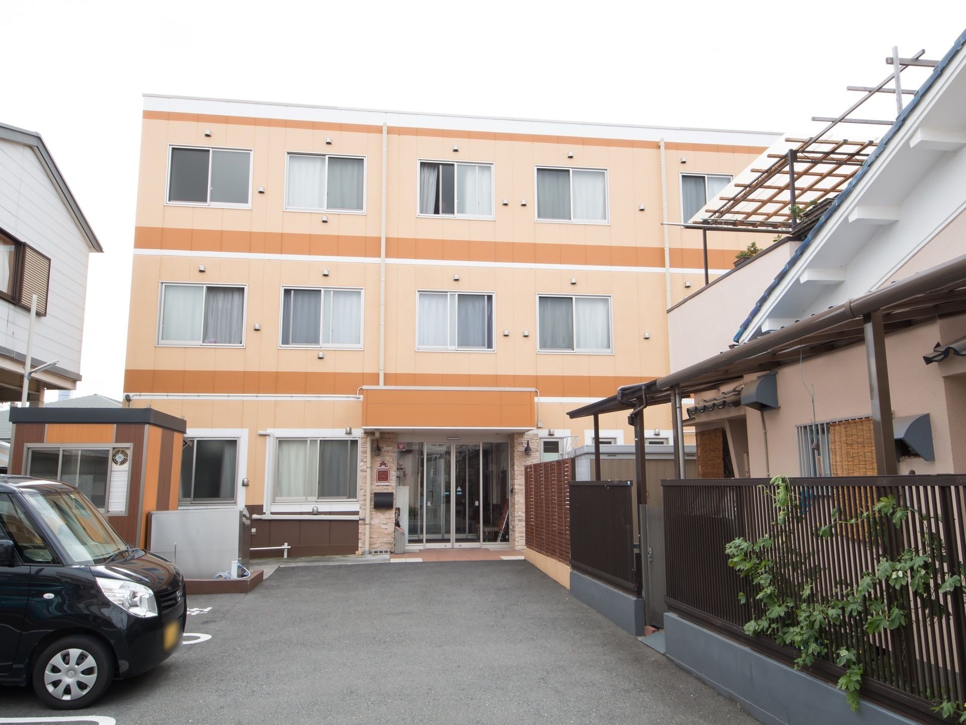 オレンジ色をベースとした外観の3階建ての建物がある。施設前はアスファルトで舗装されており、駐車スペースが設けられている。