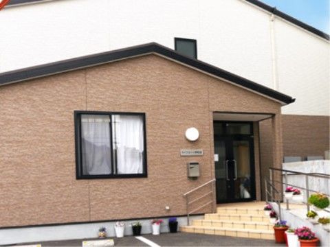 玄関前は、４段の階段とは別に手すり付きのスロープが設置されている。入口周囲には鉢植えの花が飾られている。