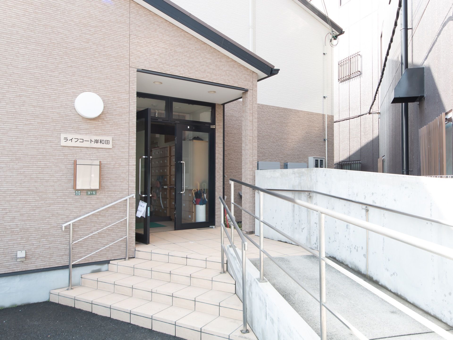 エントランスには、手すりが備えつけられた階段とスロープが設けられている。玄関扉上には、ひさしがついている。