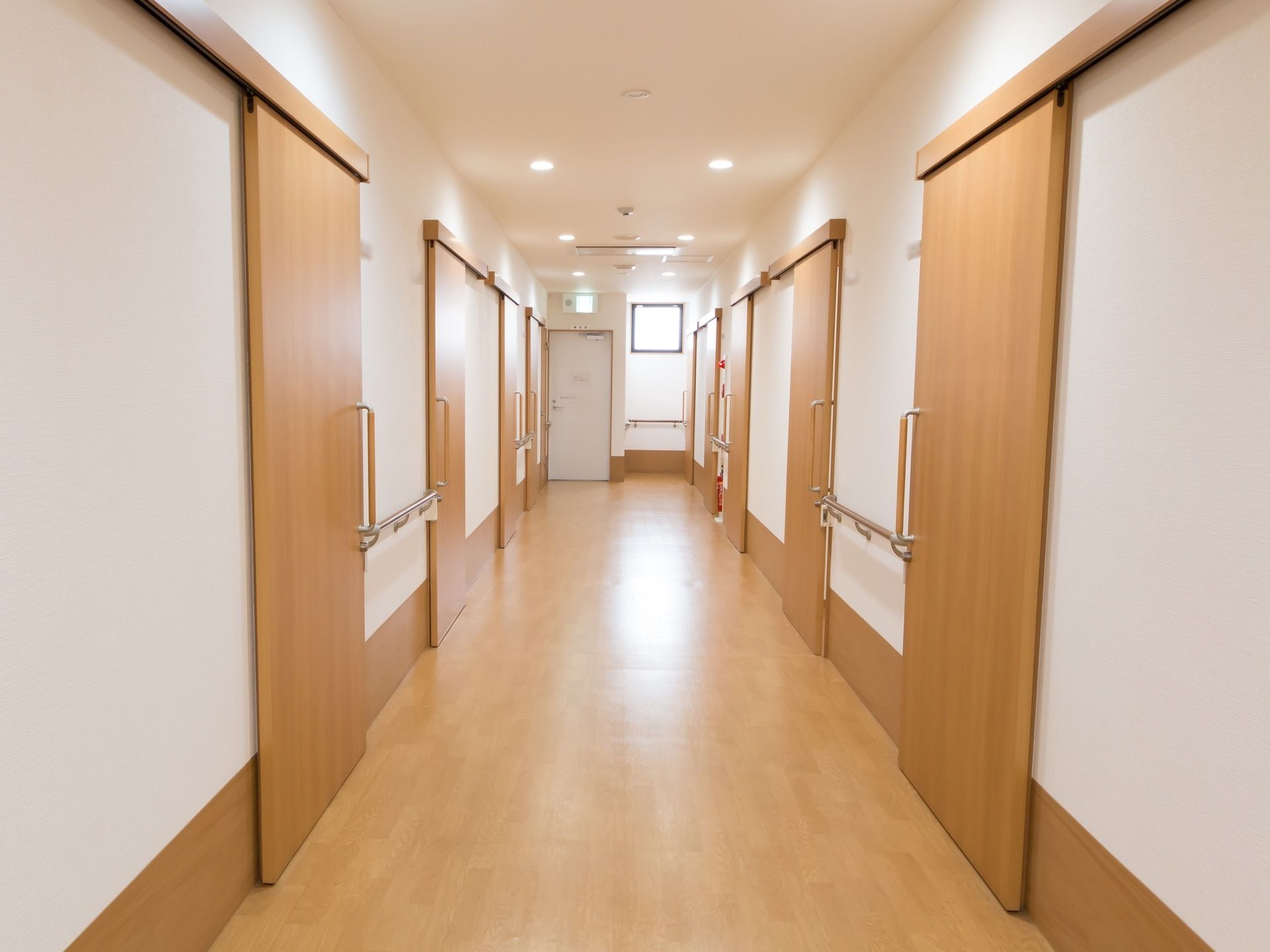 明るく広々とした廊下である。両サイドには各居室が設けられており、手すりや消火器が壁に設置されている。