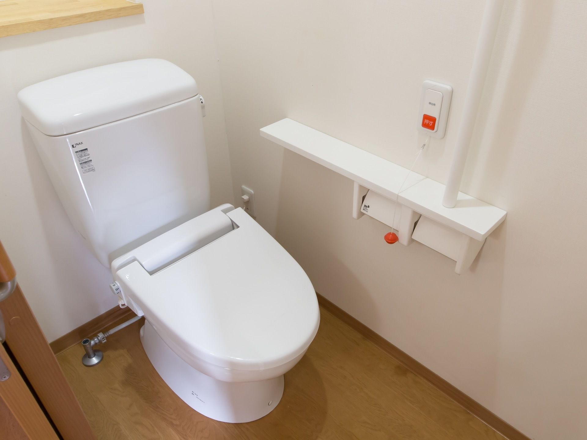 居室のトイレである。I型手すりや呼び出しボタン、備品を置ける棚が備わっている。扉には、スライドドアが採用されている。