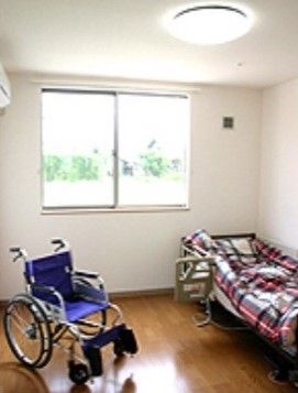 居室には窓があり、窓際には布団がセットされたベッドがある。ベッドには柵が取り付けられている。横には車椅子が置かれている。