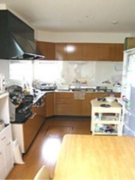入居者様のお食事を用意するL型キッチンがある。冷蔵庫の前には食事を運ぶワゴンが置かれている。近くには茶色いテーブルがある。