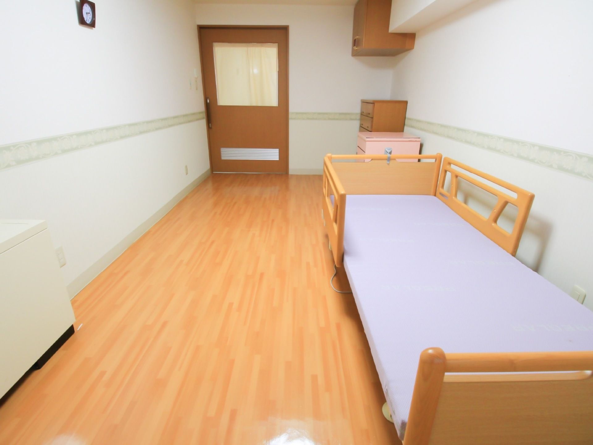 全体は白系統、床と家具は木調でまとめられている。入口は段差のない引き戸である。温水暖房機と介護用ベッドが備えつけられている。