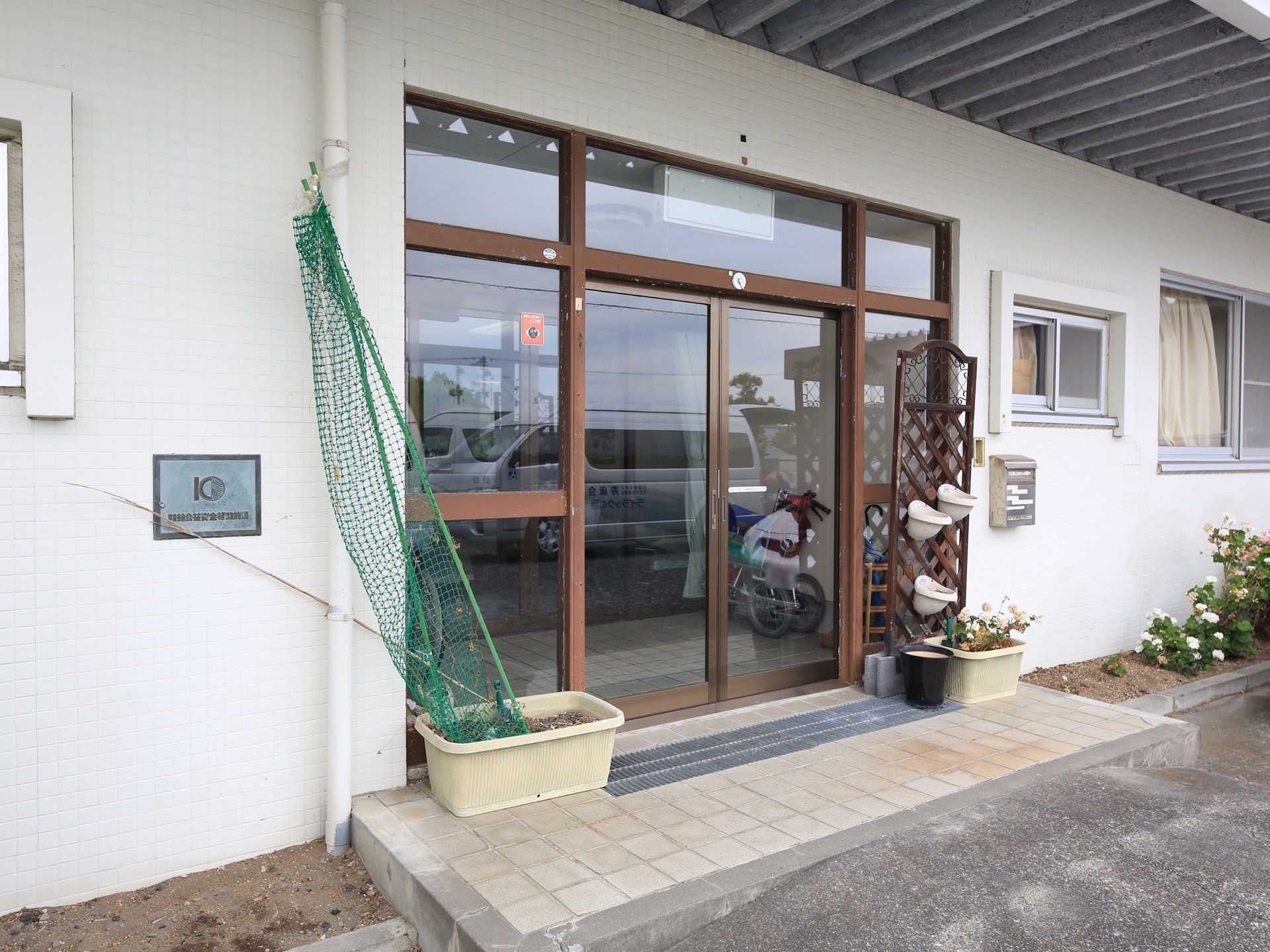 玄関の外側には、鉢植えが取りつけられたラティスやプランターが置かれている。施設の周囲には花壇がある。