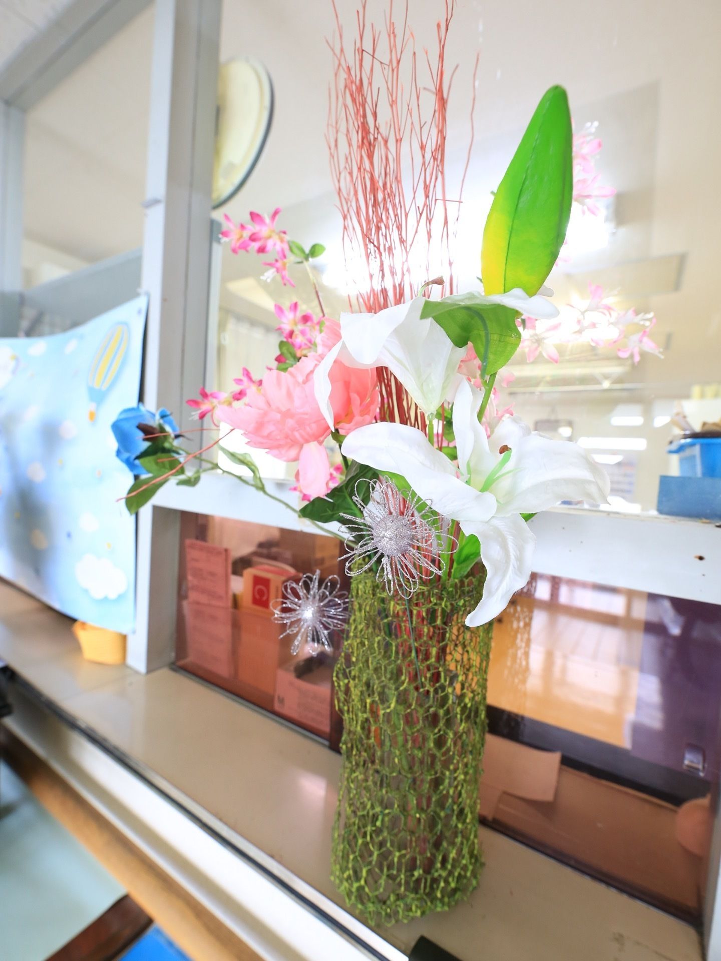 造花が飾られた事務所の窓口付近。黄緑色のワイヤーネットで、さまざまな形状の造花をくるむことによって、花瓶のように自立させている。