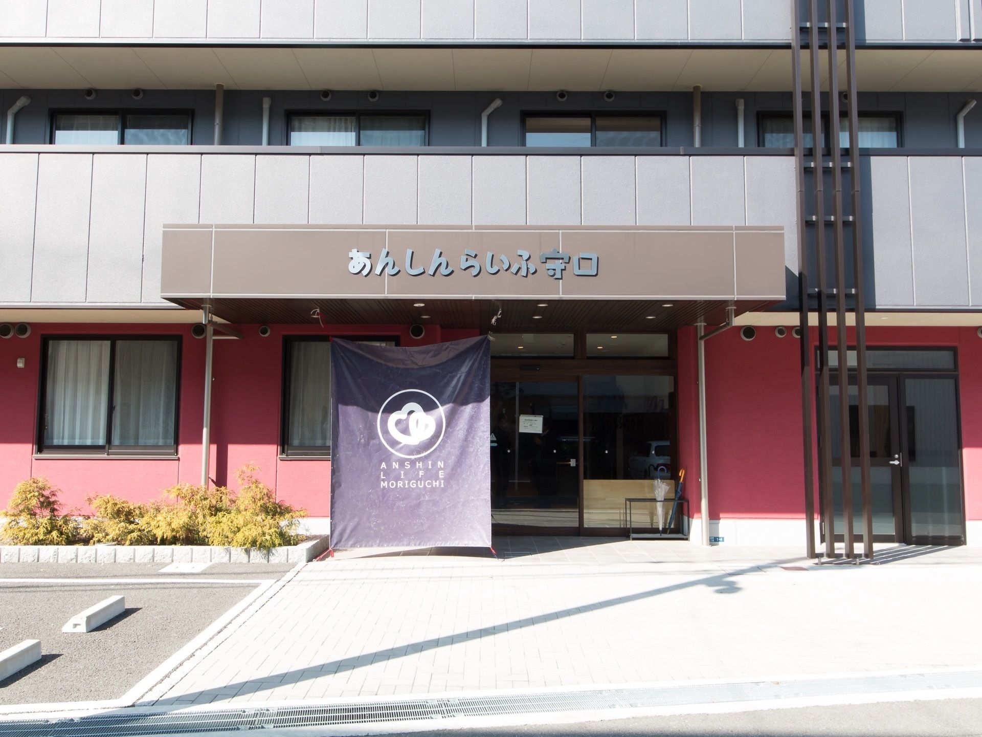 赤と黒を基調としたデザイン性のあるスタイリッシュな建物である。エントランス前には、花壇が設置されている。
