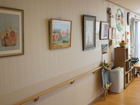 廊下の壁に、いくつもの額縁に入れられた絵画が飾られている。入居者様が描かれた絵画などを展示している。