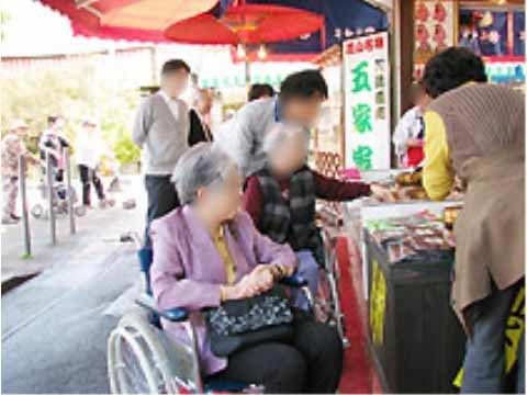 スタッフの介助を受けながら土産物屋の前で買い物をする車いすの女性二人