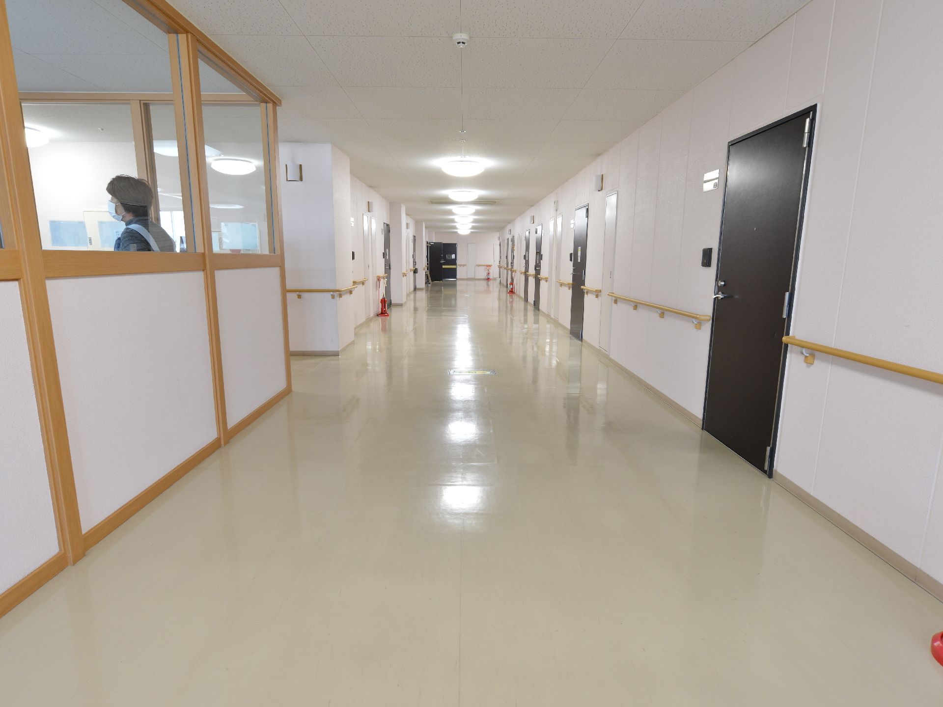 明るい色調を使用した広々とした廊下。廊下に面したガラス張りのスタッフルームがある。車椅子の移動にもスムーズな広さも十分ある。