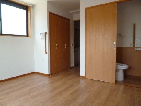 手すりが設置されたトイレと引き戸タイプの備え付けのクローゼットがある個室