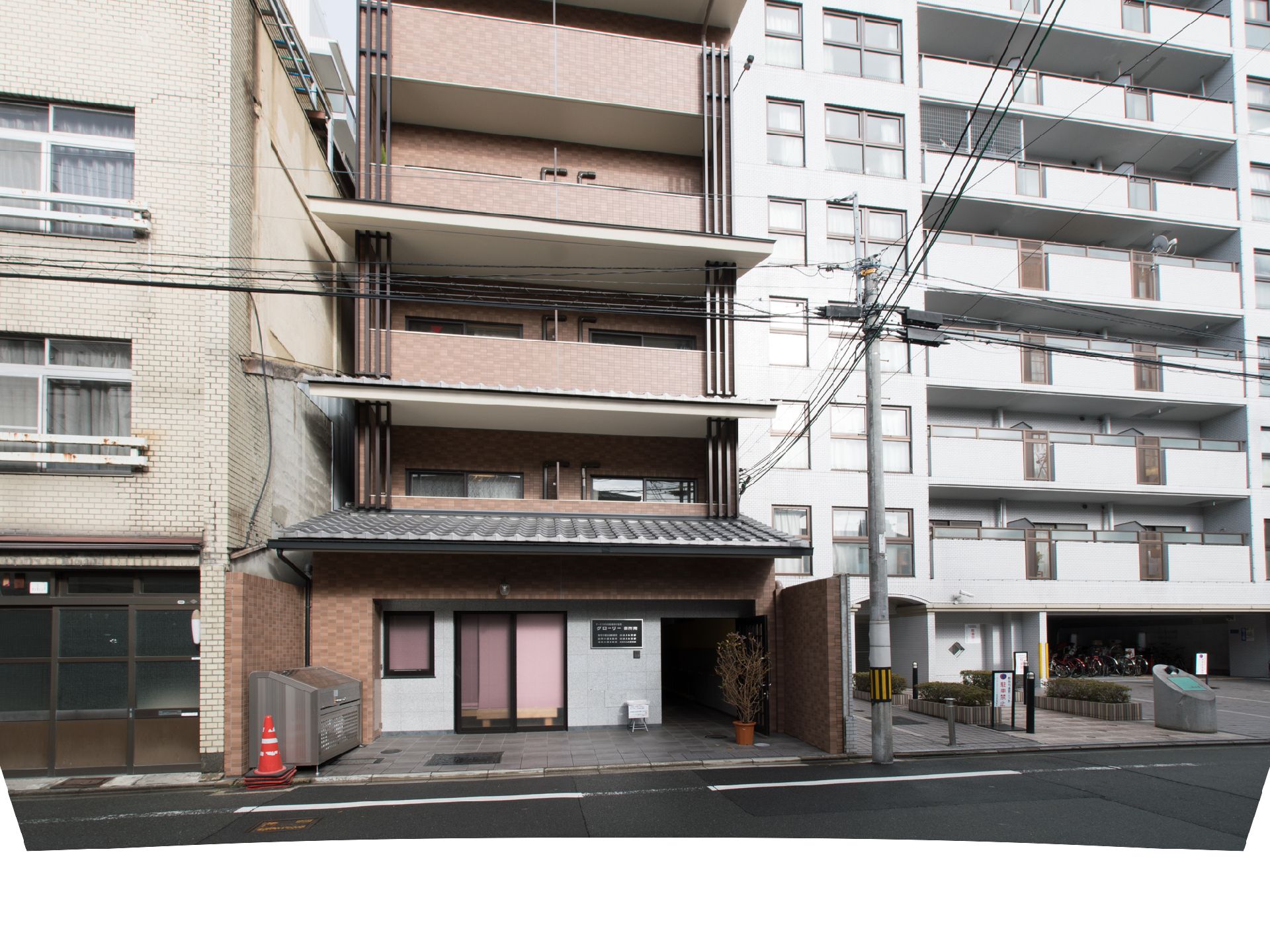 施設建物は片側と背後にマンションが隣接しており、通りに面して建っている。1階の正面にふたのあるスチール素材のゴミ置場が設置されている。