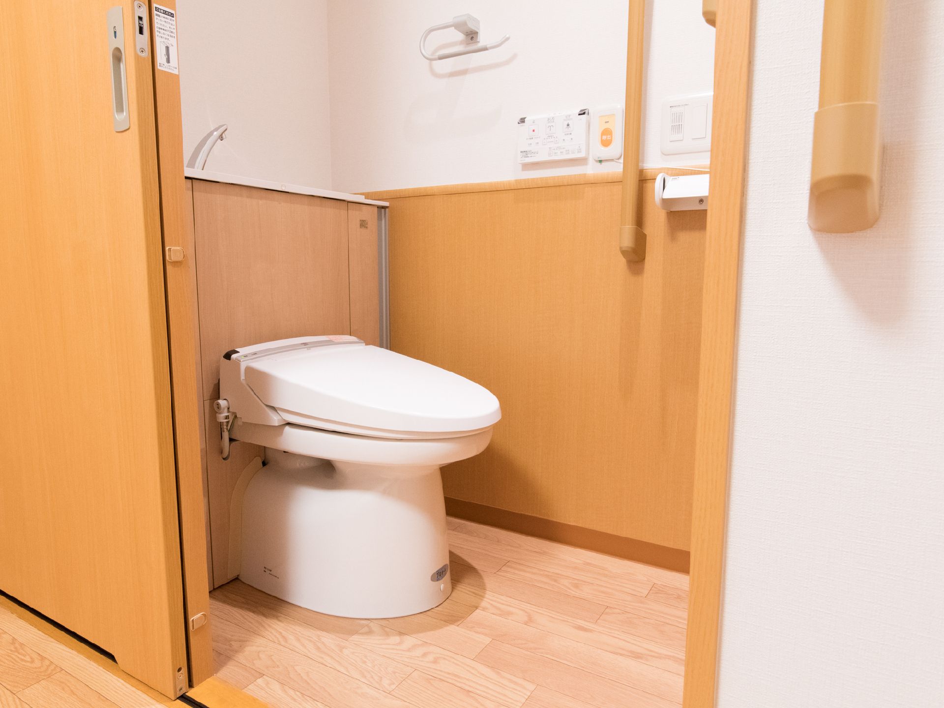 引き戸を開けるとウォシュレット付き洋式トイレがあり、外にも内側にも手すりが設置されている。座ると左手に呼び出しボタンがついている。
