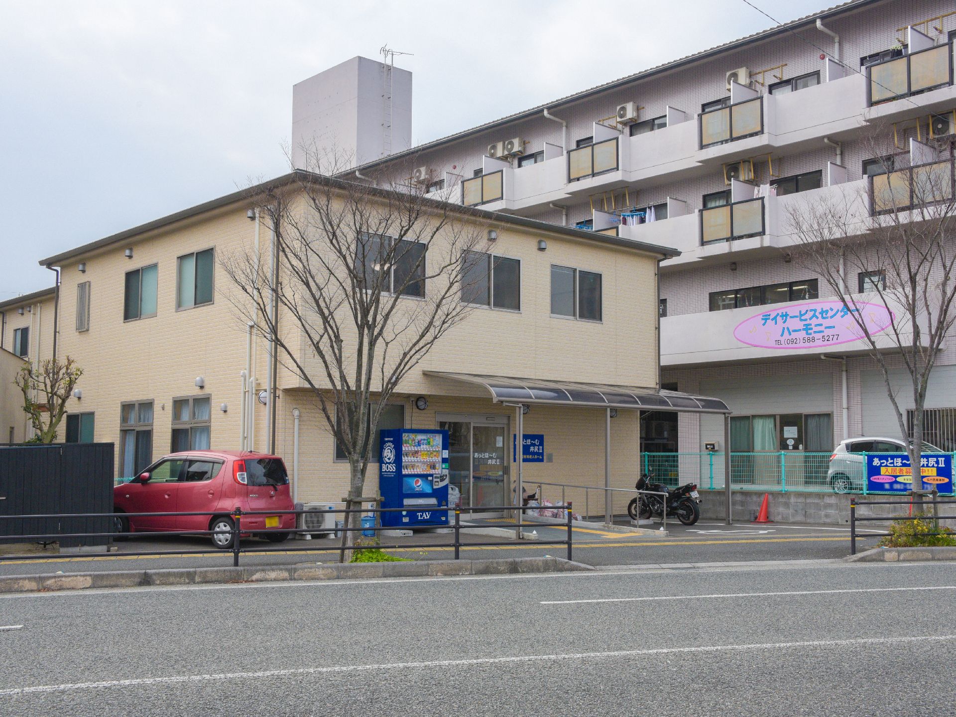 施設建物はクリーム色で自動車の通る広めの道に面している。正面に駐輪場、バイク置き、優先駐車スペースを含んだ小さい駐車場がある。