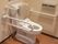 トイレは水洗トイレになっている。壁には手すりがあり、便器の横にも可動式の手すりが設置されている。タンク部分に背もたれも外付けされている。
