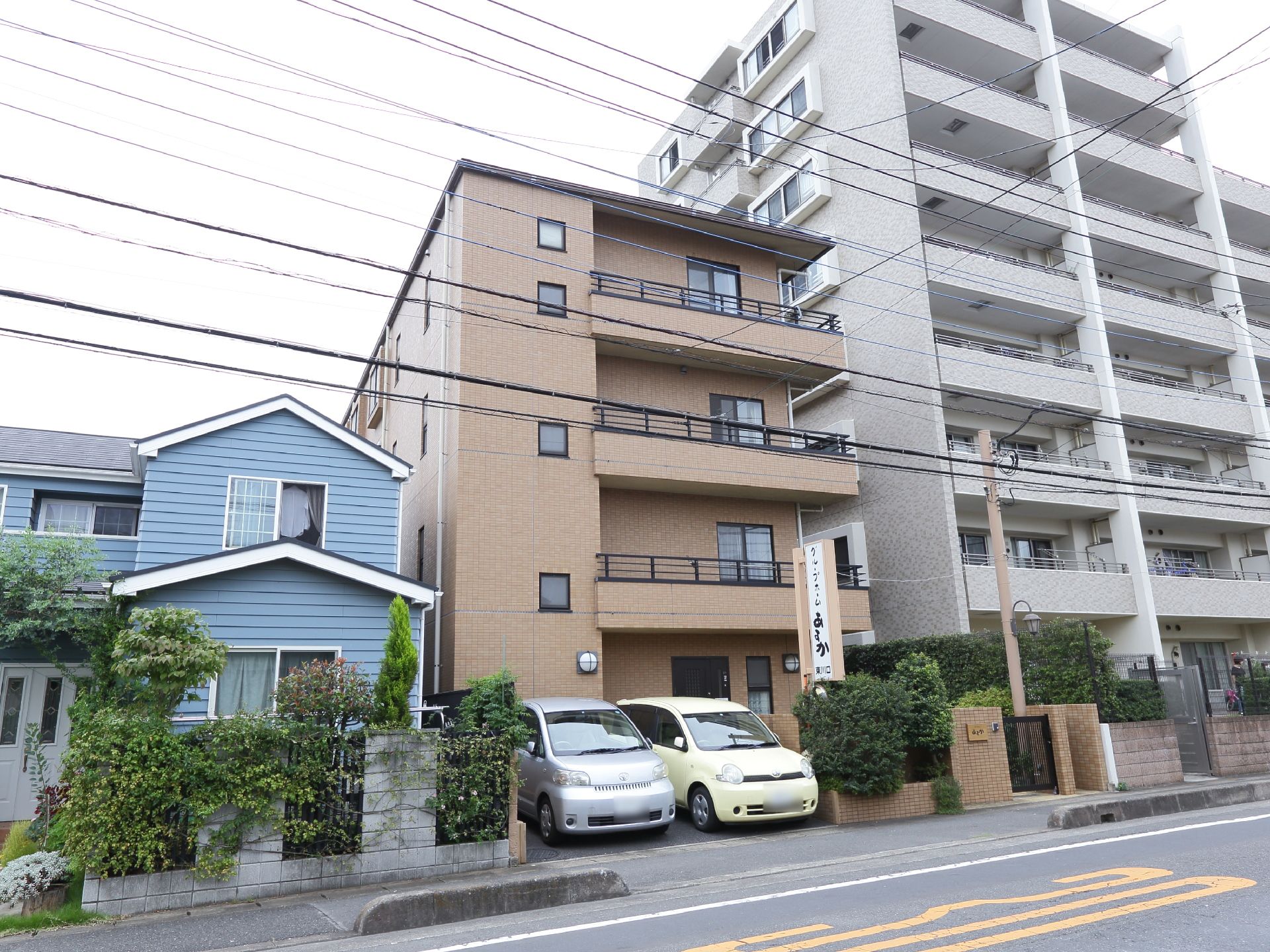 建物が横並びに建っている。施設はそれらの中央にあり、そばには看板が掲げられている。手前には道路が通っている。