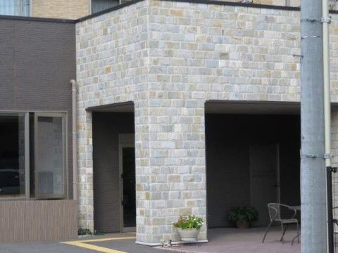 石を用いた重厚感のあるエントランス。大きな屋根の横のスペースには、鉢植えやガーデン用の椅子が置いてある。