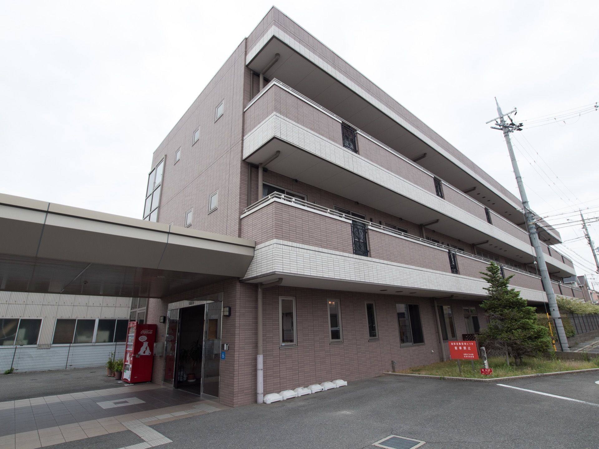３階建ての建物で玄関ポーチには屋根がある。玄関前は車が入れるスペースとなっている。入口横に自動販売機がある。