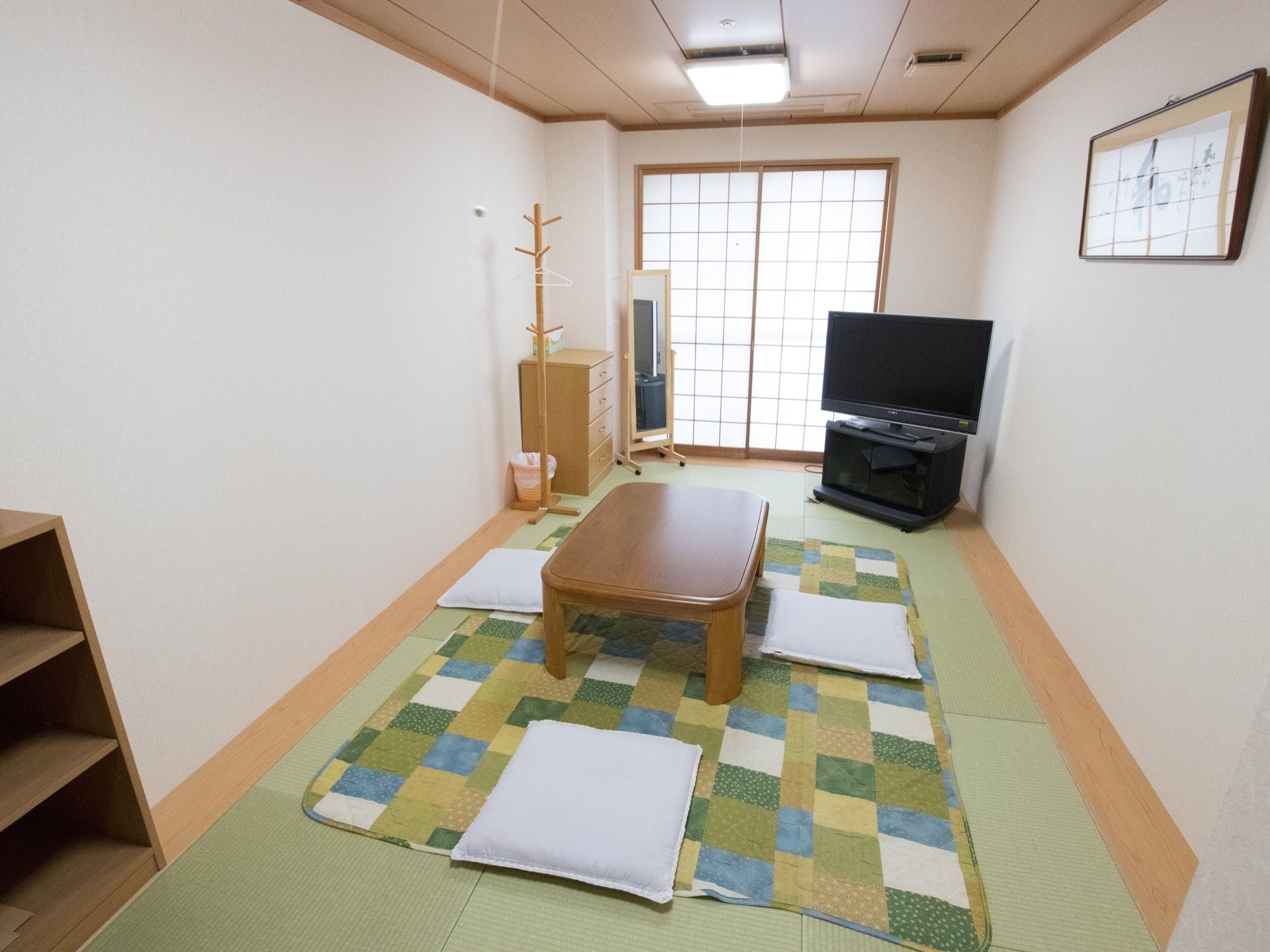 和室タイプの居室を別角度から見ると壁に額縁に入った絵が飾られ、窓は障子がはめられている。姿見が置かれている。