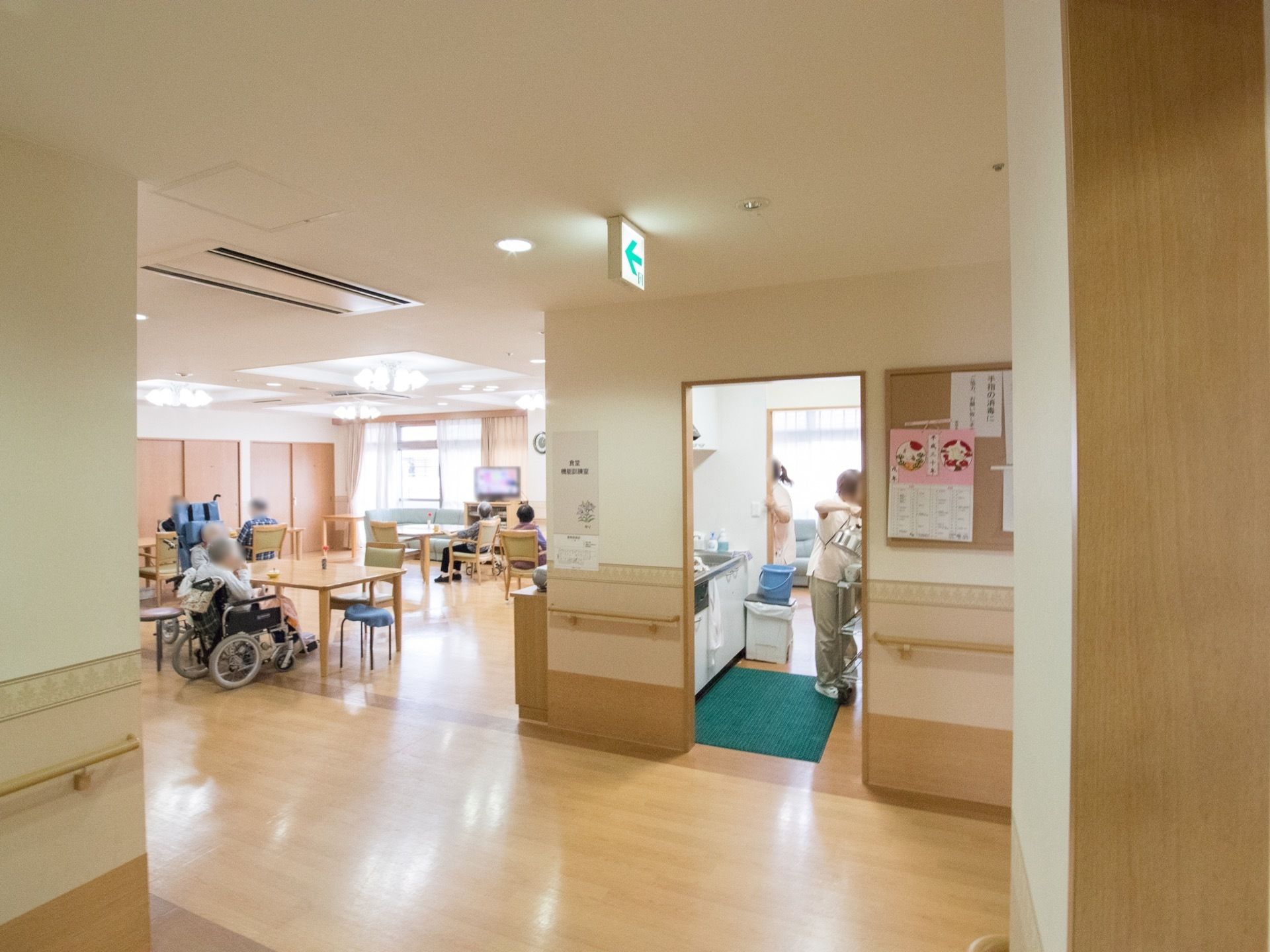 廊下の壁には手すりが設置されている。共有スペース横にスタッフの事務所があり、廊下の壁には施設からのお知らせなどが貼りだされている。
