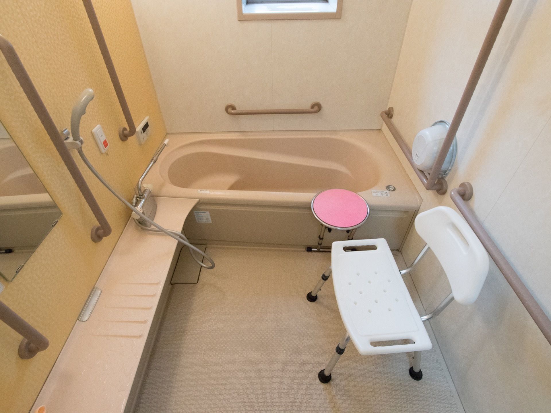 個浴用浴室の一例。壁には手すりと非常用ボタンが設置されている。洗面器と背もたれつき椅子が用意されている。