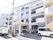 道路に面した、白い４階建ての建物である。中央に屋根付きの玄関がある。建物傍には、自転車や施設専用の車を停めている。