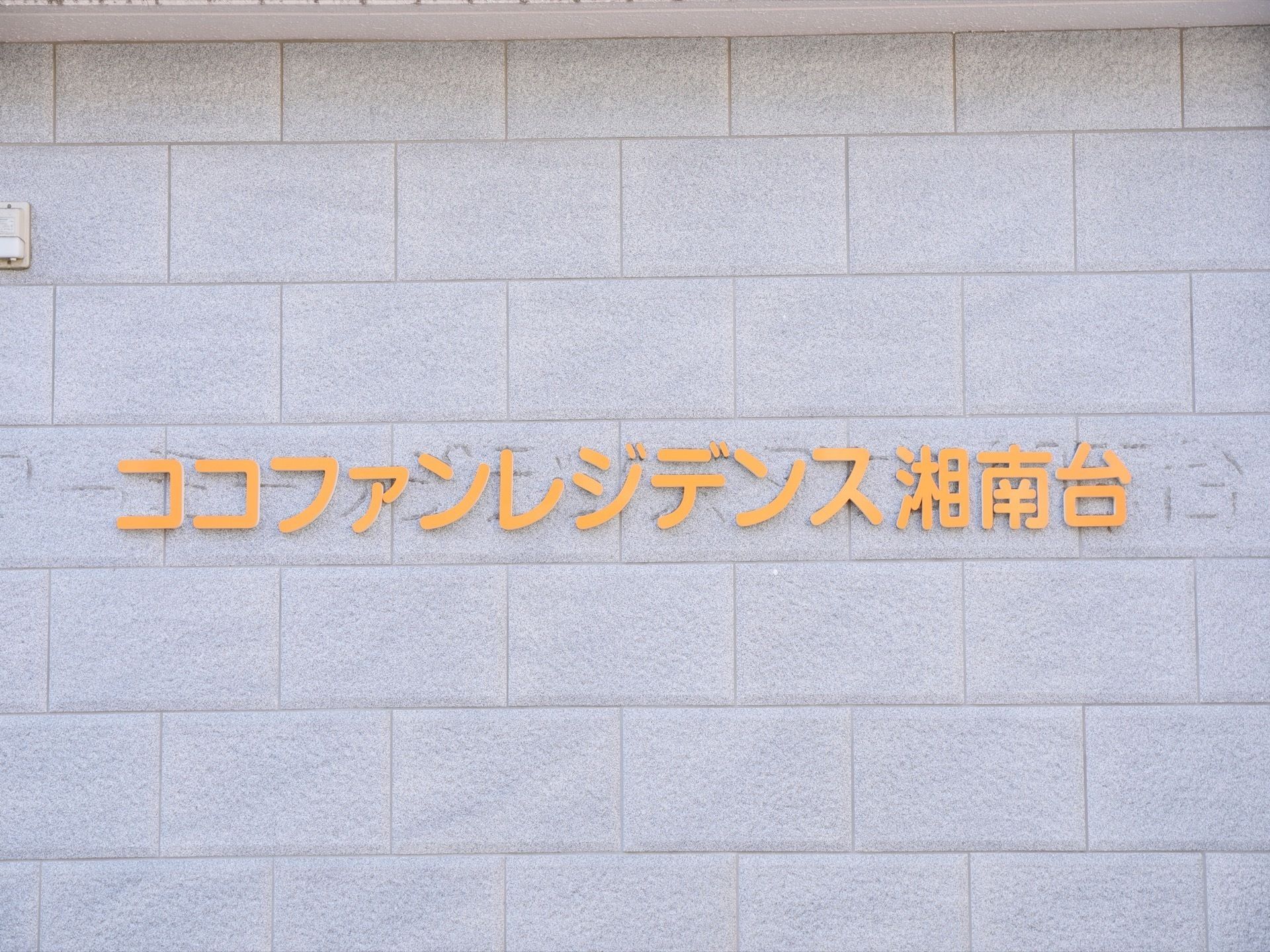 白色のタイルにオレンジ色の大きい文字で書かれた看板