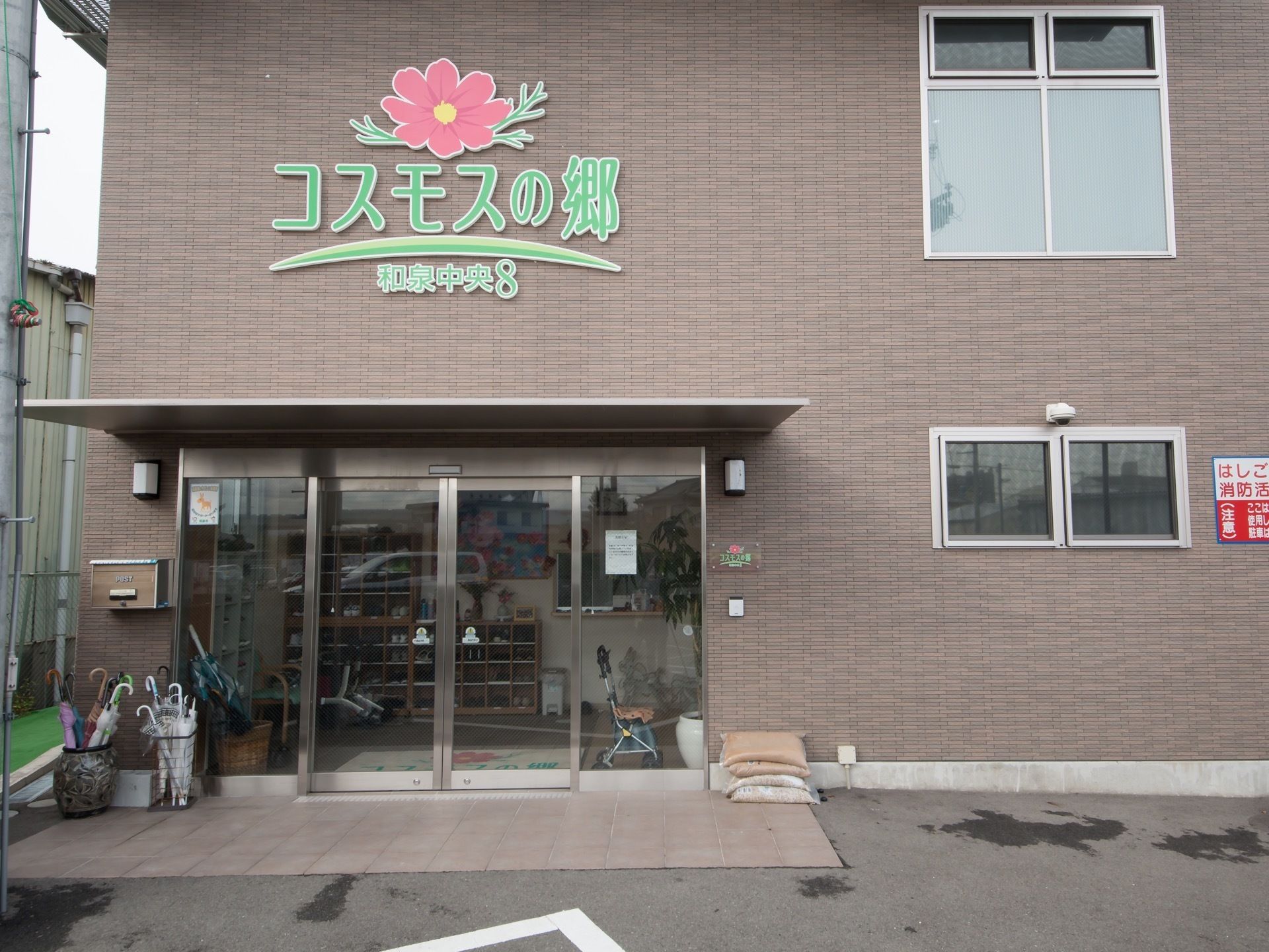 施設入口の自動扉の上部には屋根が取りつけられている。施設名称がデザインロゴマークとともに設置されている。