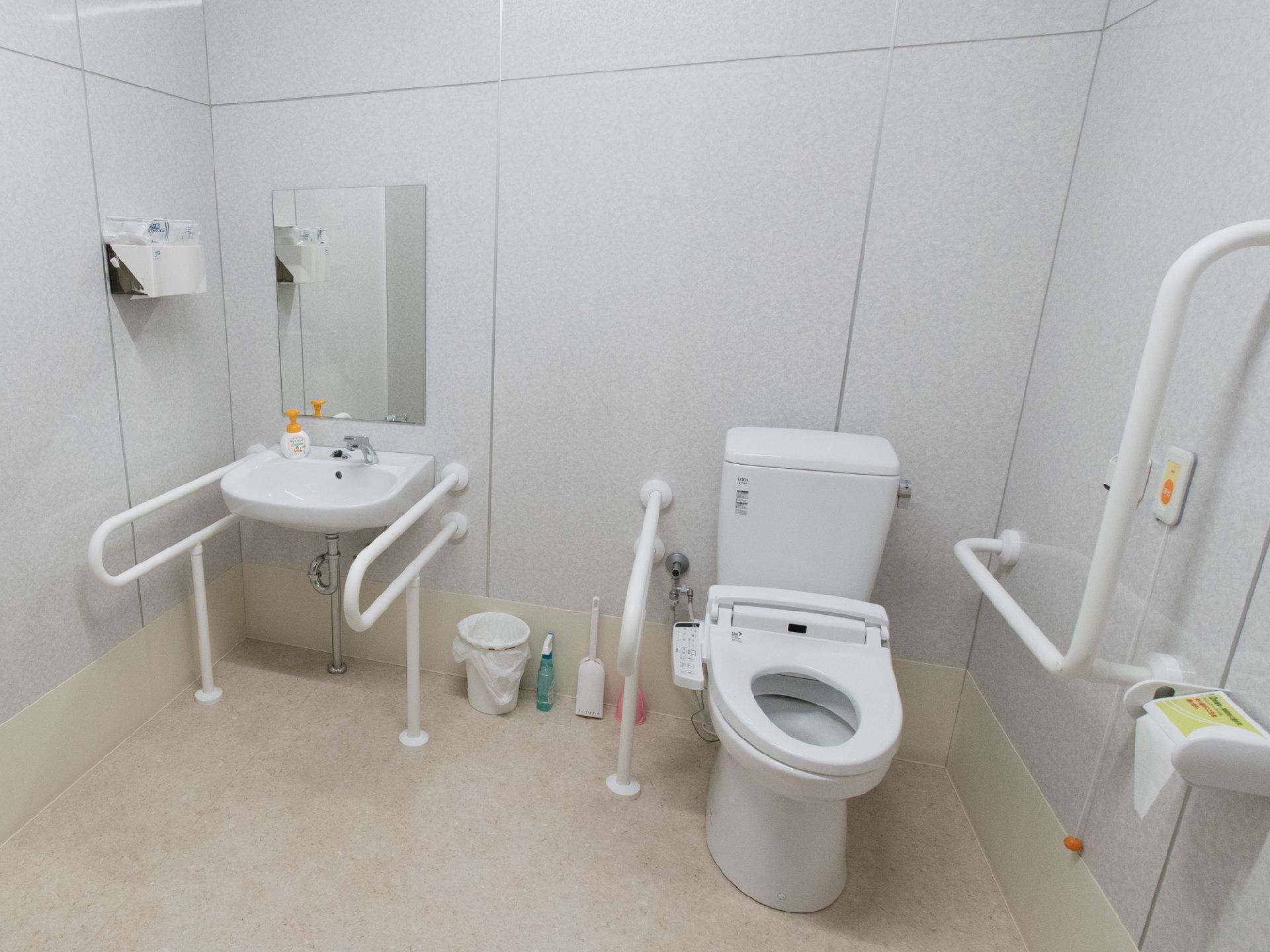 施設には介護用のトイレも設置されている。中は広く、ウォシュレットのトイレと洗面台、壁には手すりと呼び出しスイッチがあり床にも手すりがある。