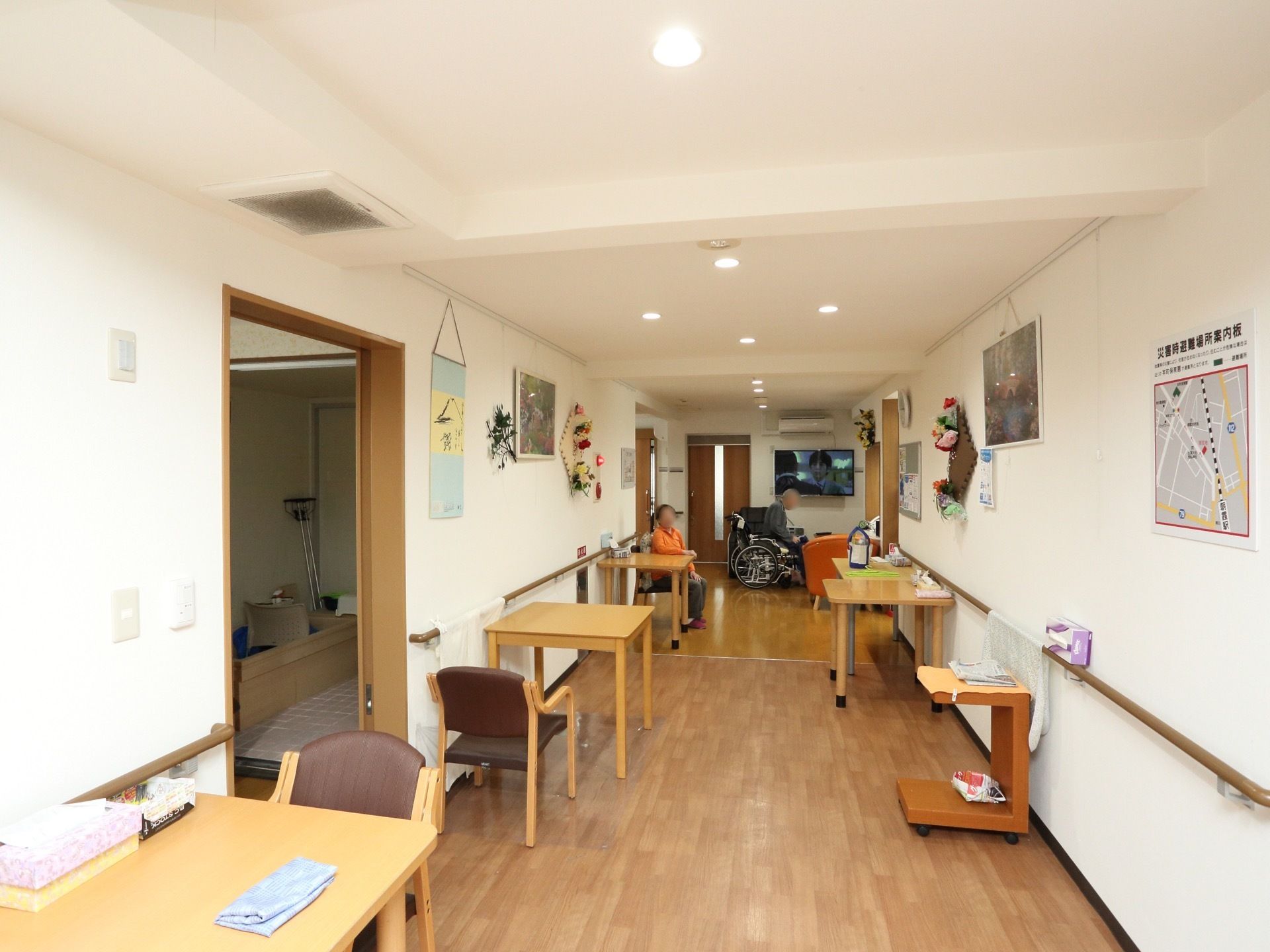 広々とした通路である。両側に木製テーブル、椅子が複数配置されている。壁には絵画や花などが飾られている。