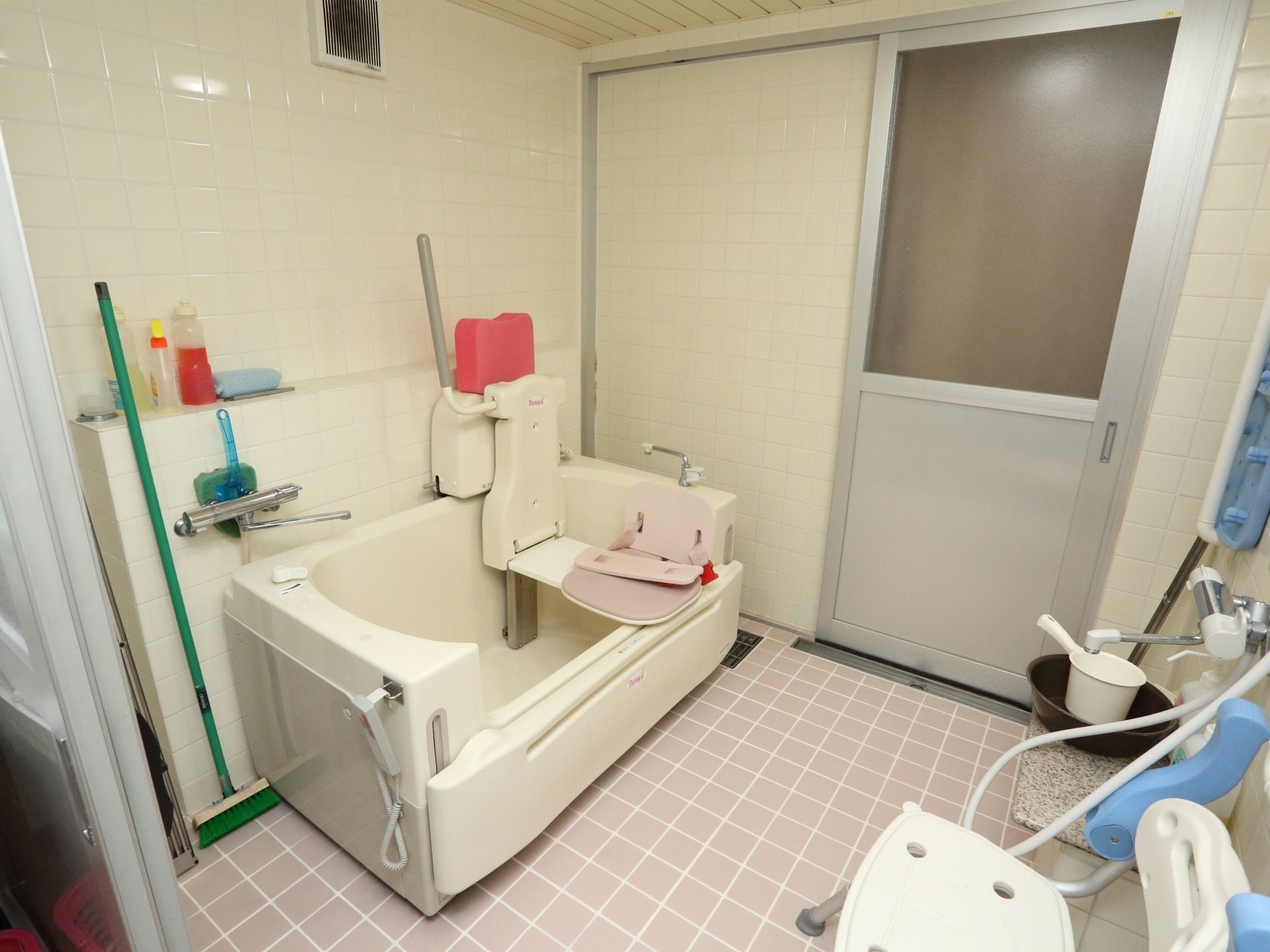 あたたかいピンク色の床、白い壁の浴室である。扉は引き戸式で、個浴型介護浴槽やシャワーチェアなどが完備されている。