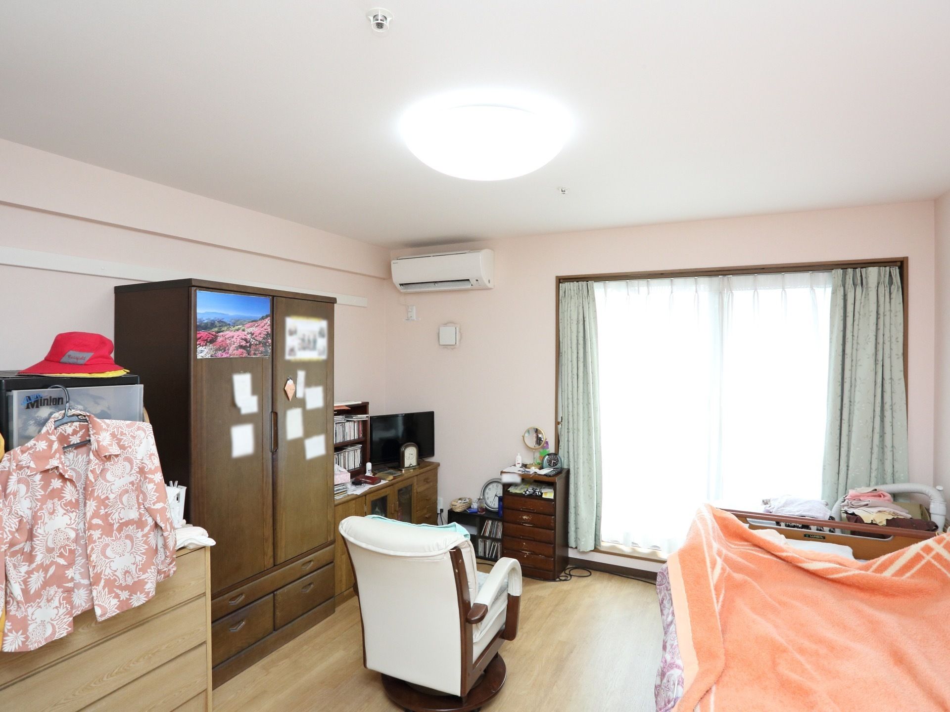 フローリングの部屋に、電動ベッド、椅子、クローゼットなどが置かれている。大きな窓があり、エアコンがついている。