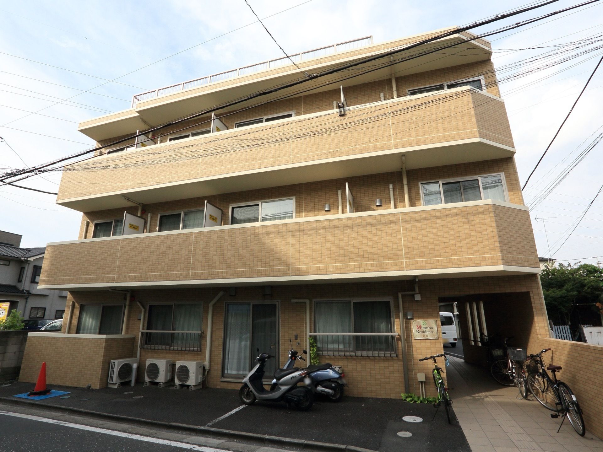 ３階建てのマンションのような外観である。入口付近には自転車やバイクが数台停まっている。各居室にはベランダがある。
