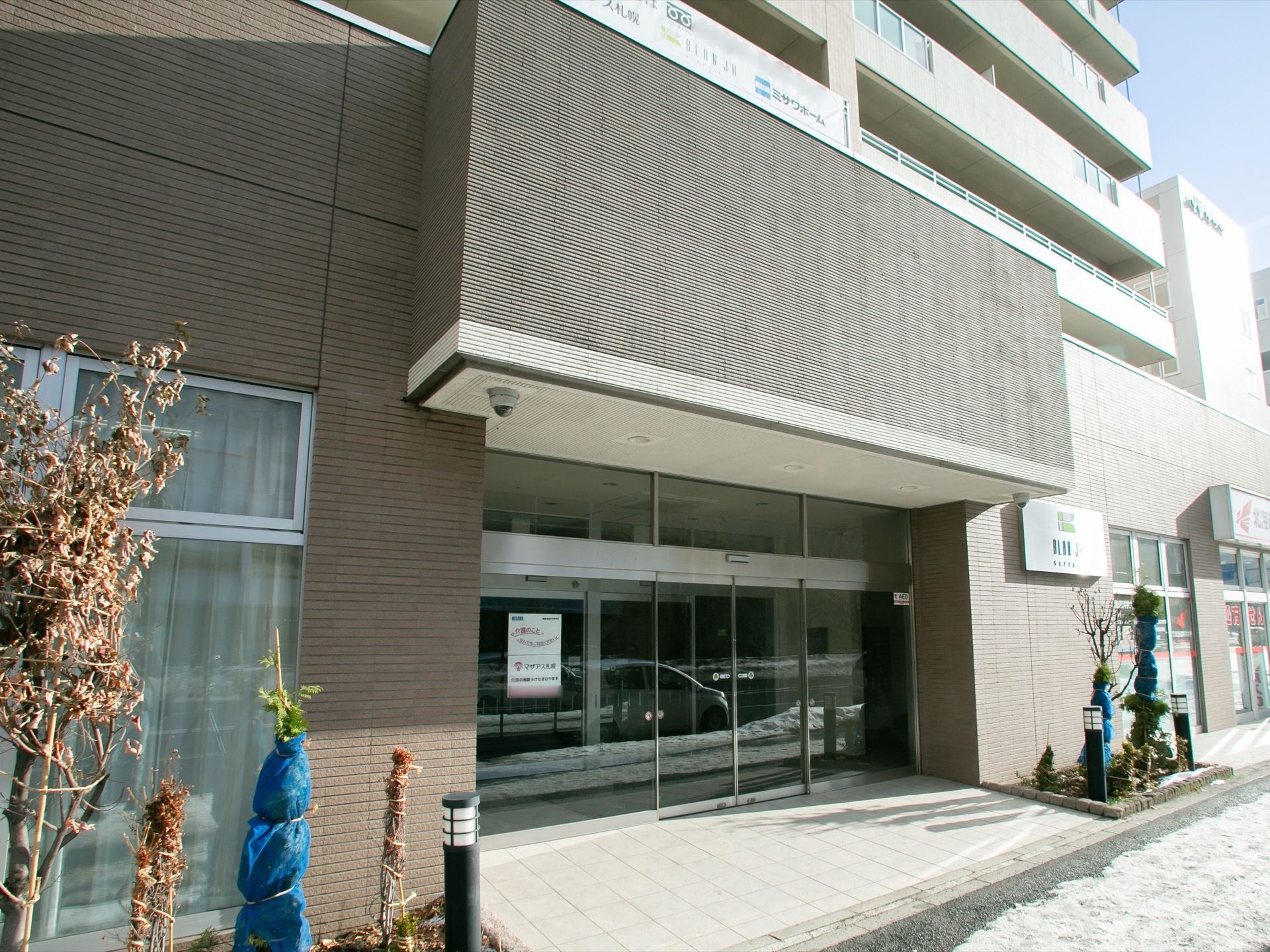 歩道と玄関までの間に段差をなくしている。大きなガラスの自動扉で、入り口前に夜間はライトアップがされる植栽が施されている。