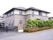 施設はブラウン系を基調とした2階建ての建物である。外周には黒いフェンスがあり、その外には背の高い樹と植え込みがある。